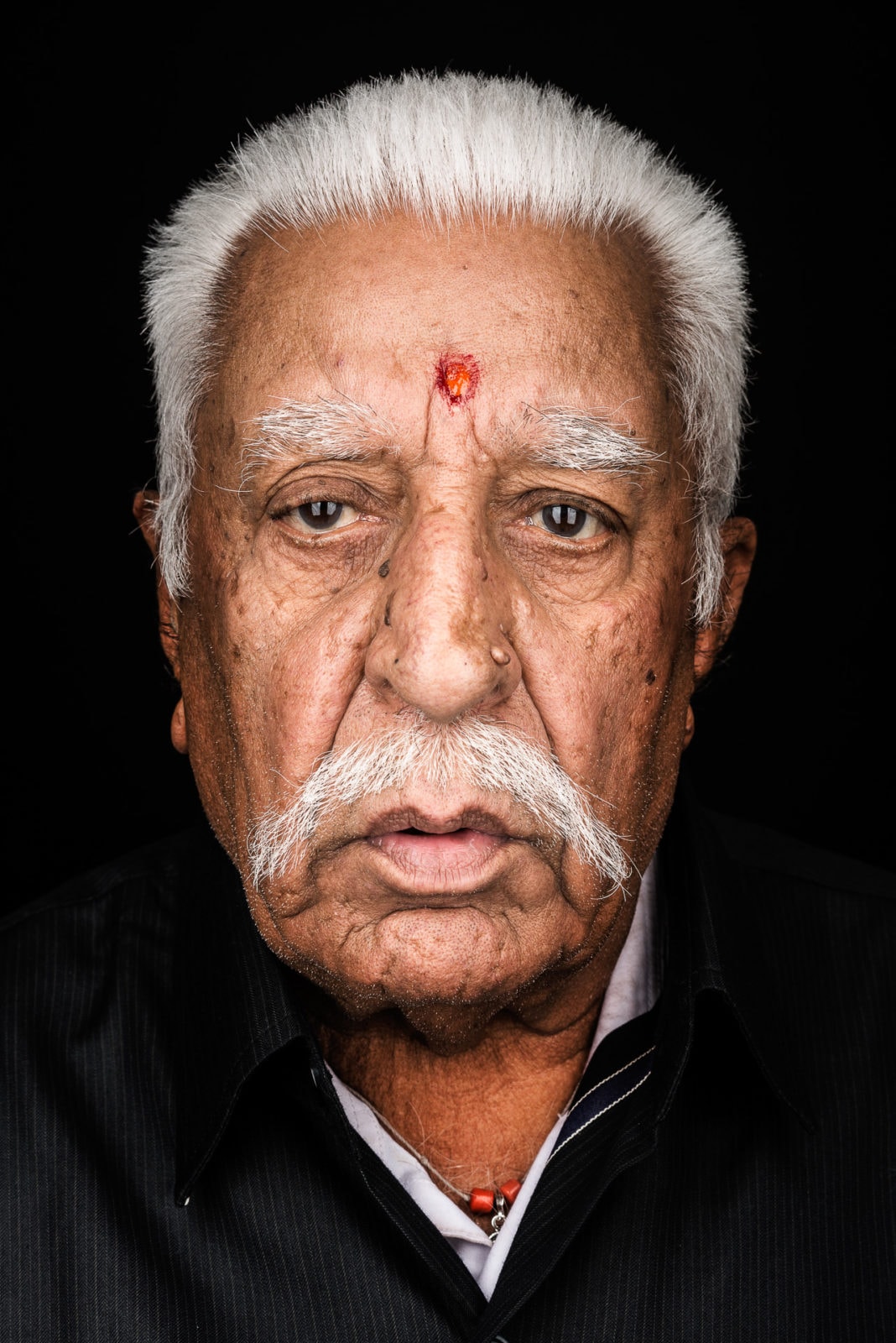 Ein indischer Mann mit weißen Haaren und schwarzem Hintergrund, porträtiert von Fotograf Markus Mielek.