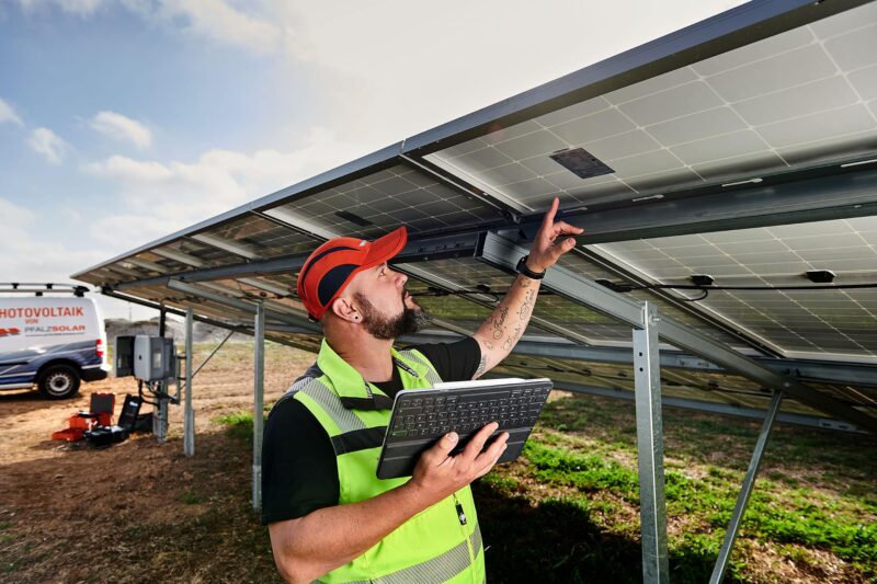 Das Mitarbeiterportrait zeigt einen Mann, der technisch versiert ein Solarpanel kontrolliert