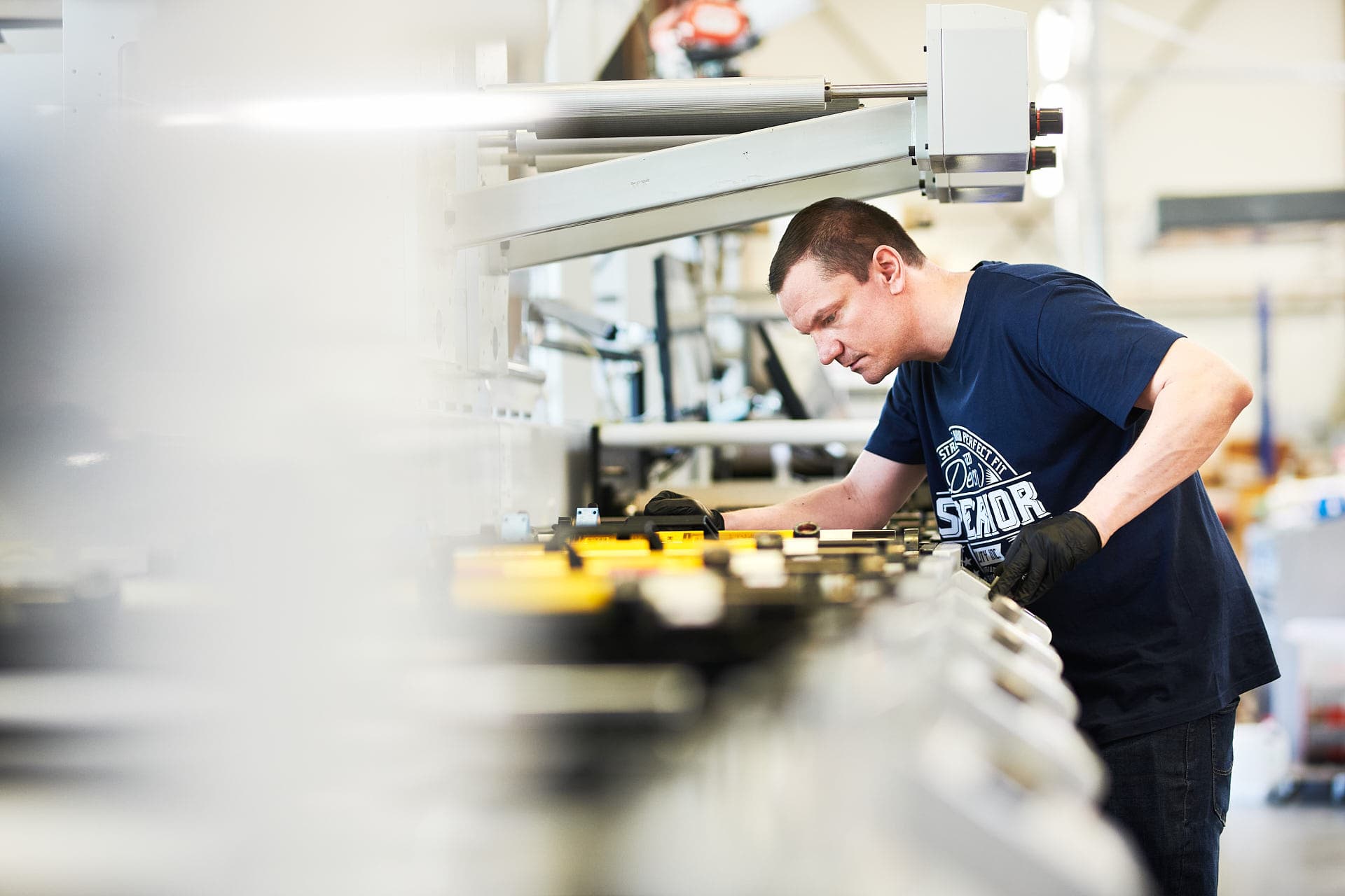 Ein Mitarbeiter überprüft für ein Portrait die Druckmaschine in den Räumlichkeiten des Unternehmes in einer großen Industriehalle