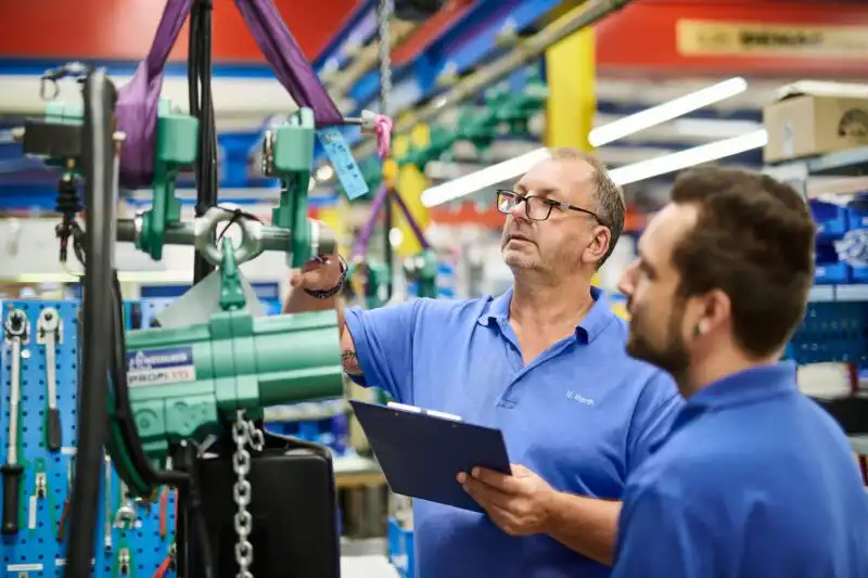 Zwei Menschen prüfen ein Produkt in einer Industrieproduktion. Das Mitarbeiterportrait zeigt die beiden Menschen am Arbeitsplatz