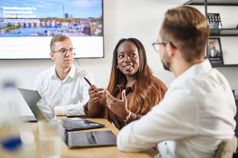 Drei Geschäftsleute in einem modernen Konferenzraum in Dortmund diskutieren während eines Businessportraits-Shootings.
