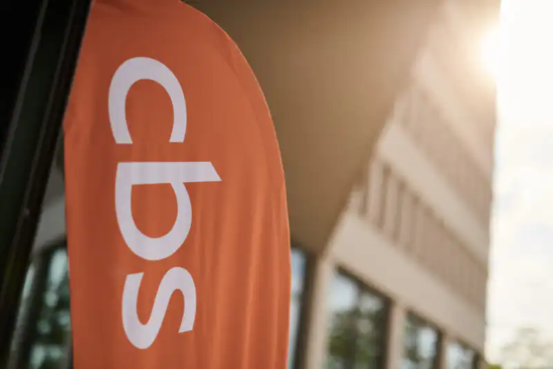Orangefarbenes CBS-Logo-Banner vor Unternehmensgebäude in Dortmund, Imagefotografie für Corporate Event im Gegenlicht.