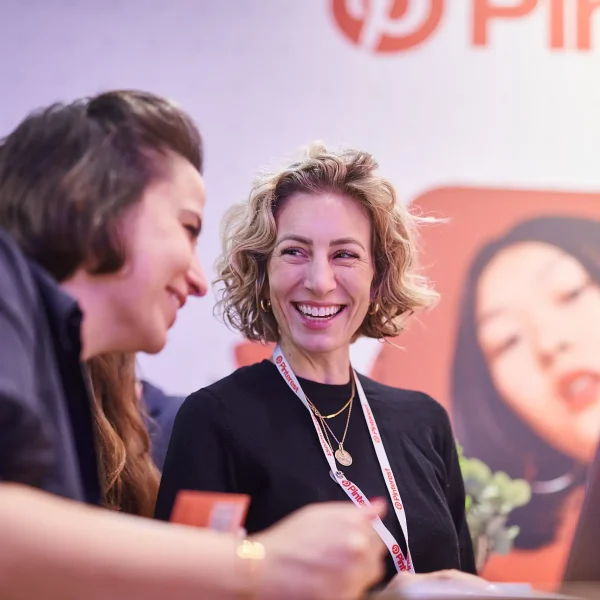 Zwei Pinterest-Mitarbeiterinnen lachen am Messestand auf der dmexco 2025 in Köln, festgehalten in der Eventfotografie.