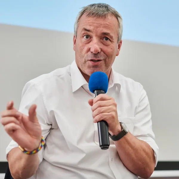 Ein Redner im weißen Hemd spricht mit blauem Mikrofon und gestikuliert, festgehalten vom Eventfotografen beim Werkstattgespräch in Dortmund.
